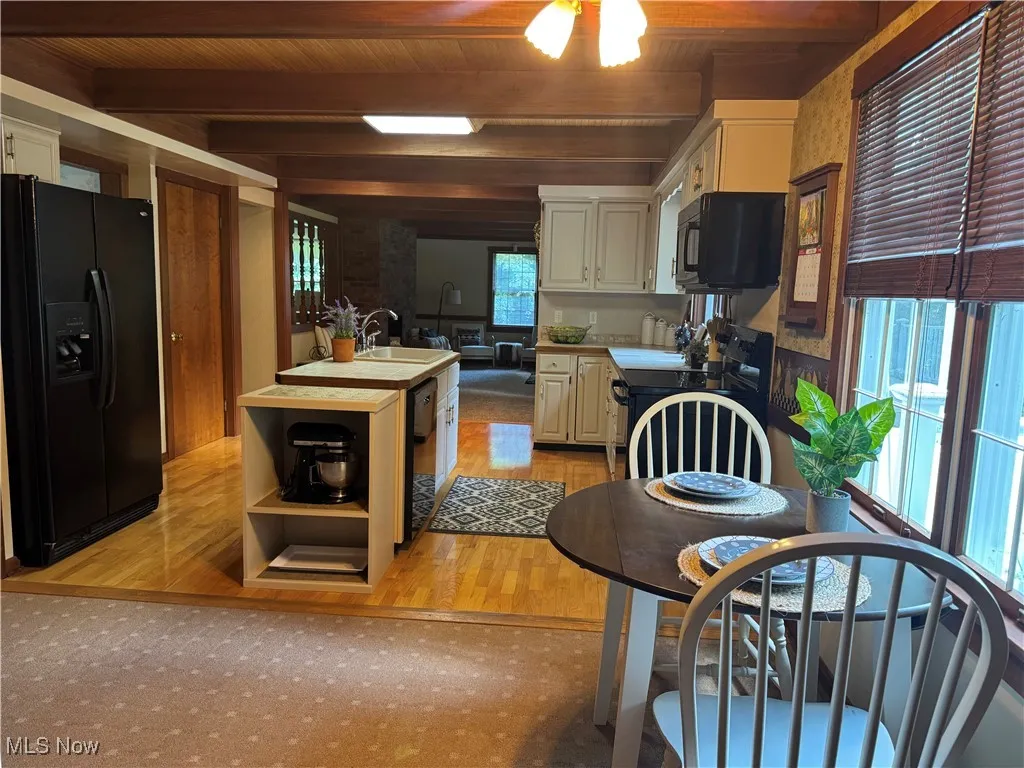 Kitchen with black appliances, a wooden ceiling with exposed beams, light wood-style floors, a center island with sink, and open shelves