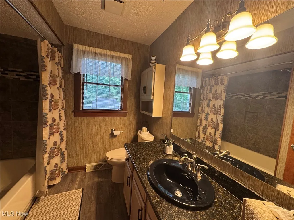 Bathroom featuring granite vanity, wood finished floors, tiled shower / bath combination with curtain, and a textured ceiling