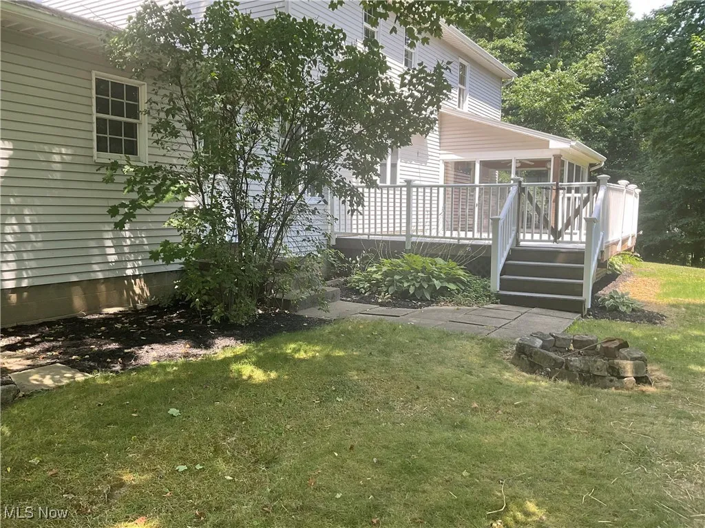 View of green lawn featuring a sunroom, a deck, and stairway