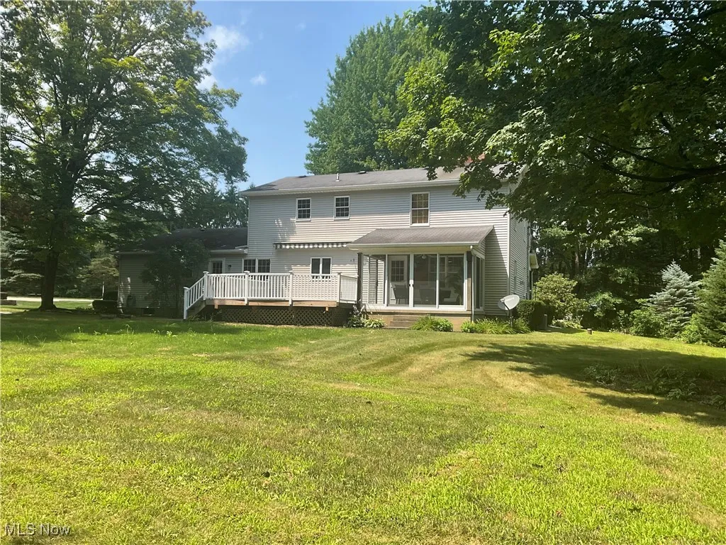 Rear view of property with a sunroom, a wooden deck, and a yard