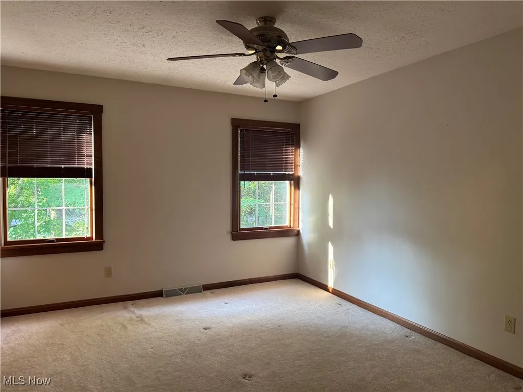 Empty room featuring carpet floors, a textured ceiling, and ceiling fan