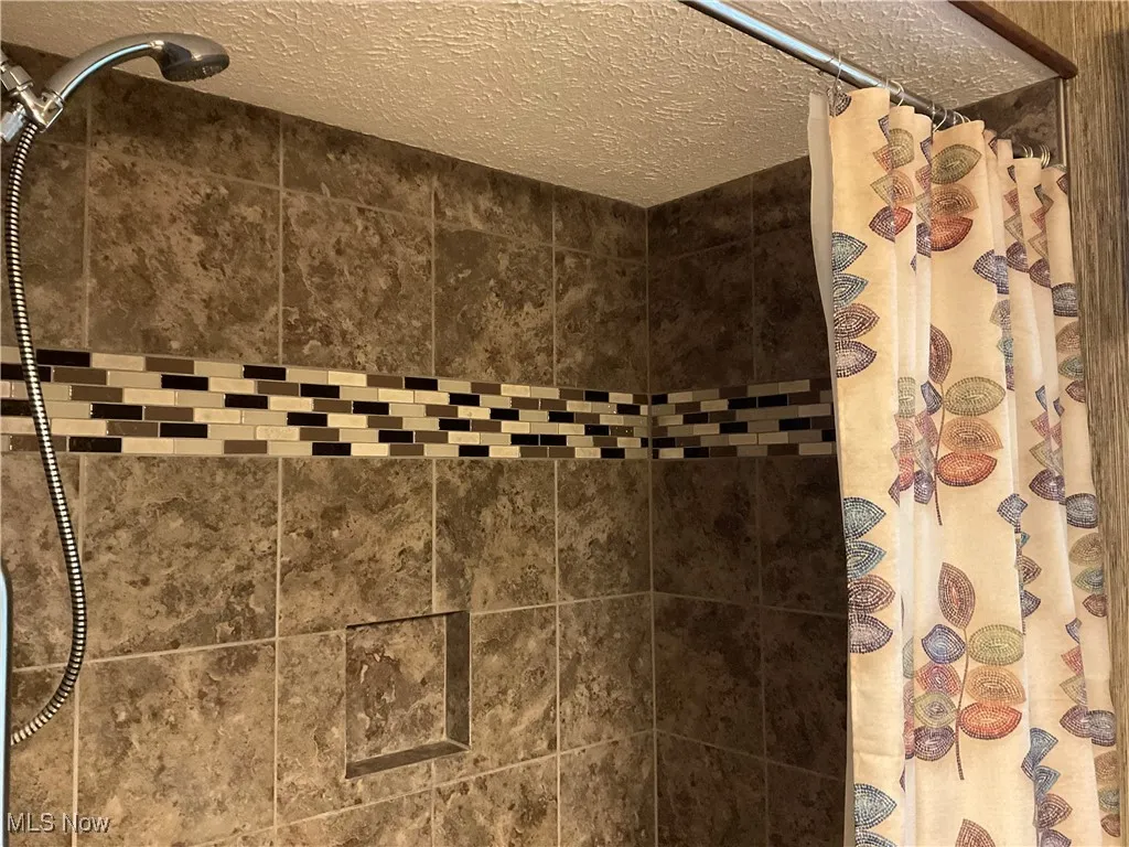 Bathroom view of a tile shower and a textured ceiling