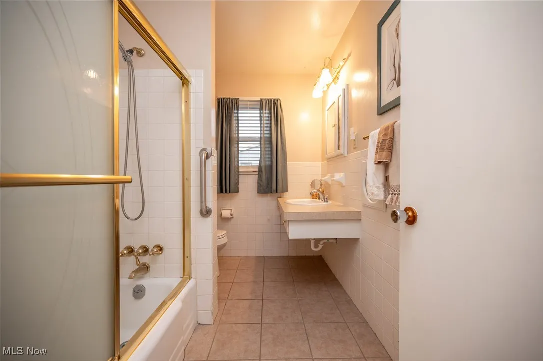 Full bath featuring tile patterned floors, tile walls, shower / bath combination with glass door