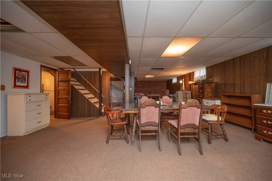Carpeted area featuring a paneled ceiling, wooden walls