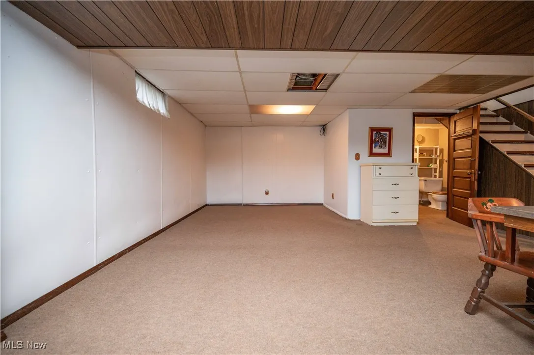 Full below grade area featuring carpet floors, stairs, and a drop ceiling