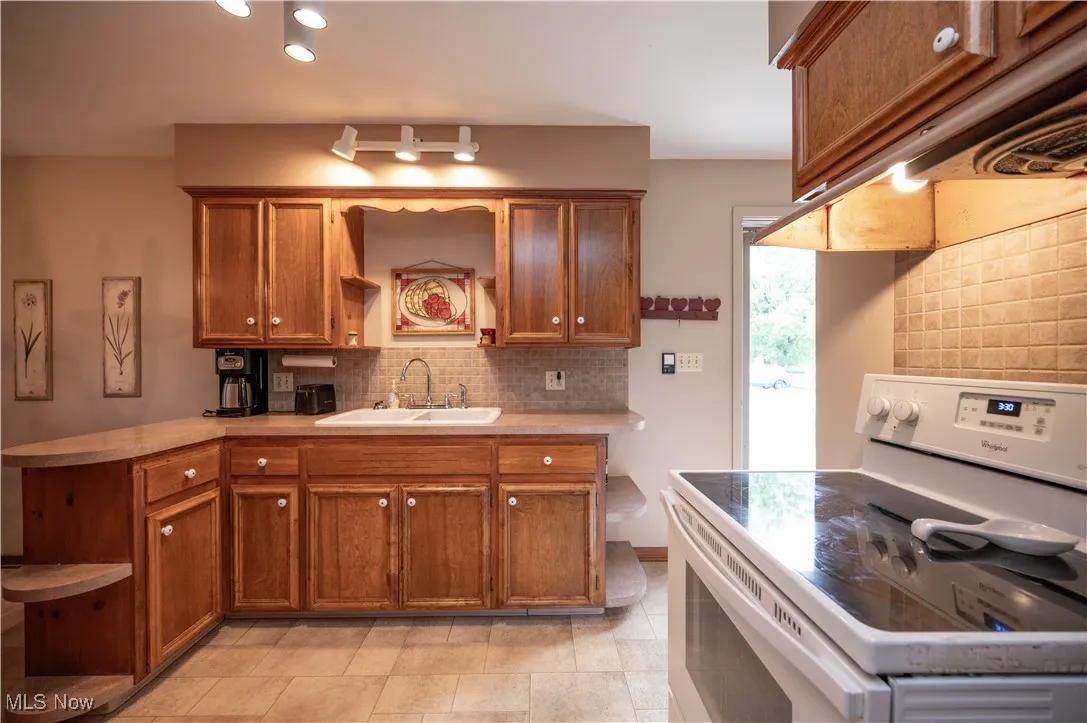 Kitchen with open shelves, white electric range oven, brown cabinetry, tasteful backsplash, and light countertops
