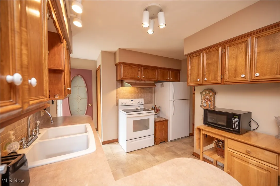 Kitchen featuring white appliances, brown cabinetry, backsplash, and light countertops
