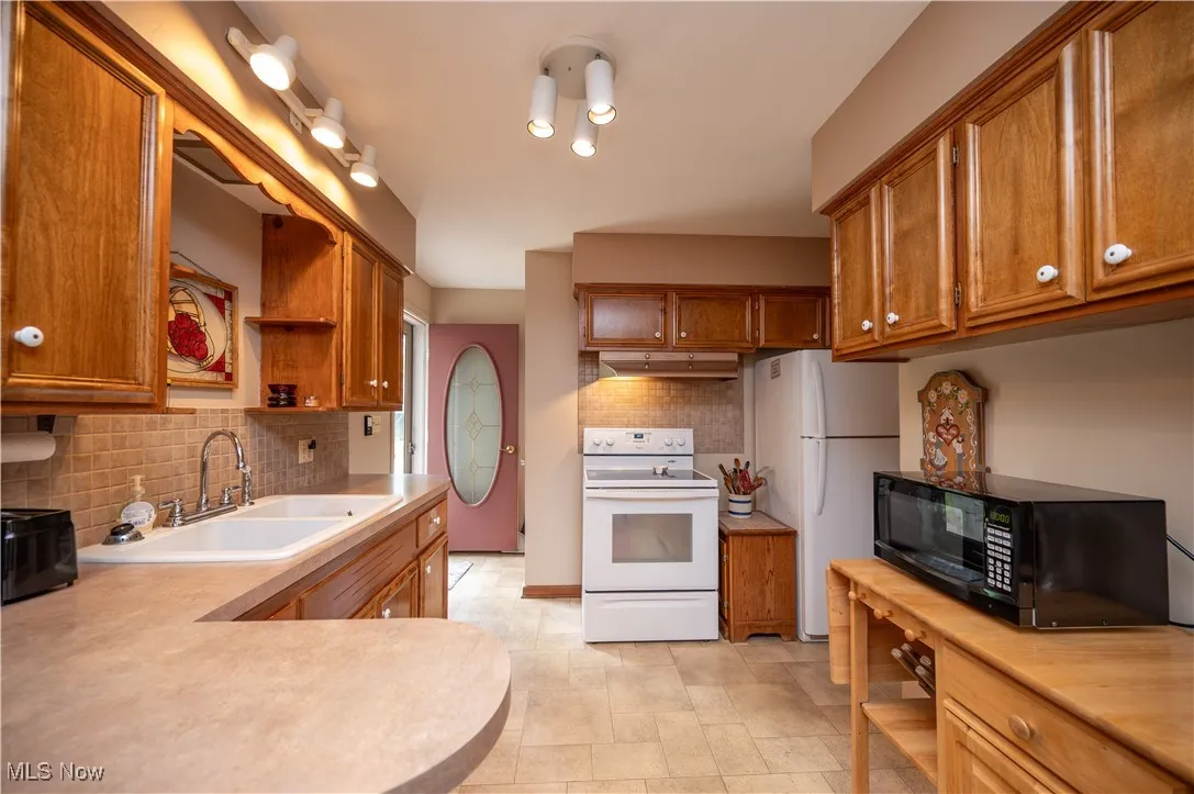 Kitchen with white appliances, open shelves, light countertops, and brown cabinetry