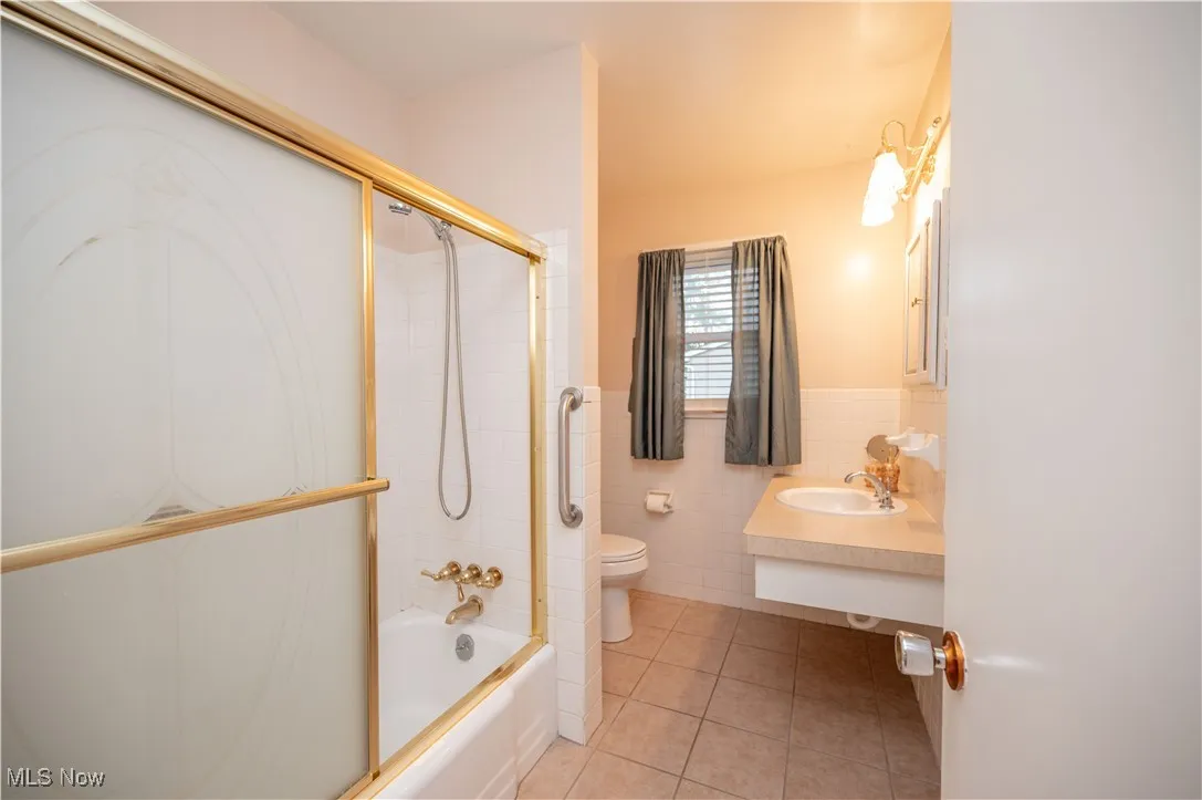 Full bathroom with tile patterned floors, bath / shower combo with glass door, tile walls, and vanity