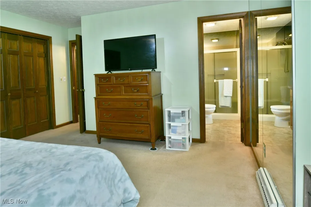 Bedroom with light carpet, ensuite bath, a baseboard heating unit, a textured ceiling, and a closet