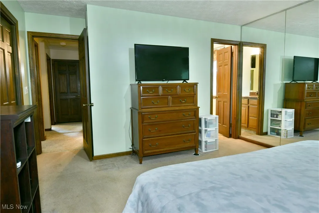 Bedroom with light colored carpet, a textured ceiling, and ensuite bathroom