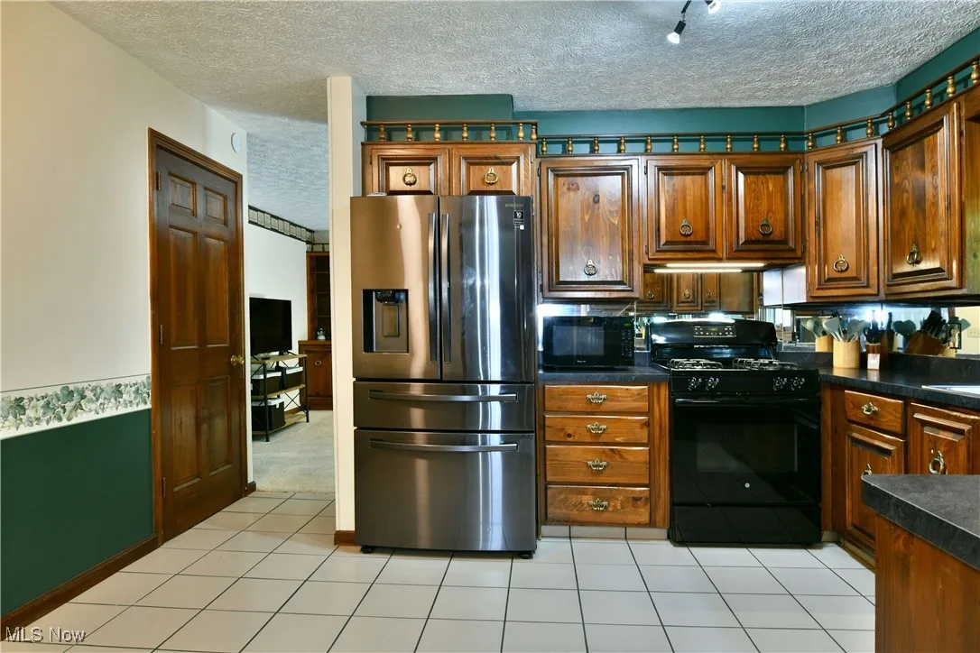 Kitchen with stainless steel fridge with ice dispenser, black gas range oven, dark countertops, a textured ceiling, and rail lighting