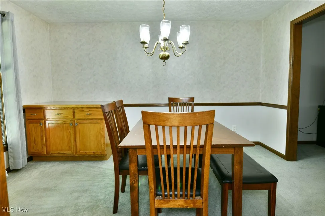 Dining area featuring light carpet, a chandelier, and wallpapered walls