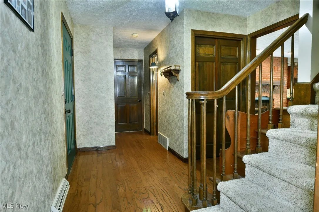 Entryway featuring stairway, wood finished floors, a baseboard heating unit, and a textured ceiling