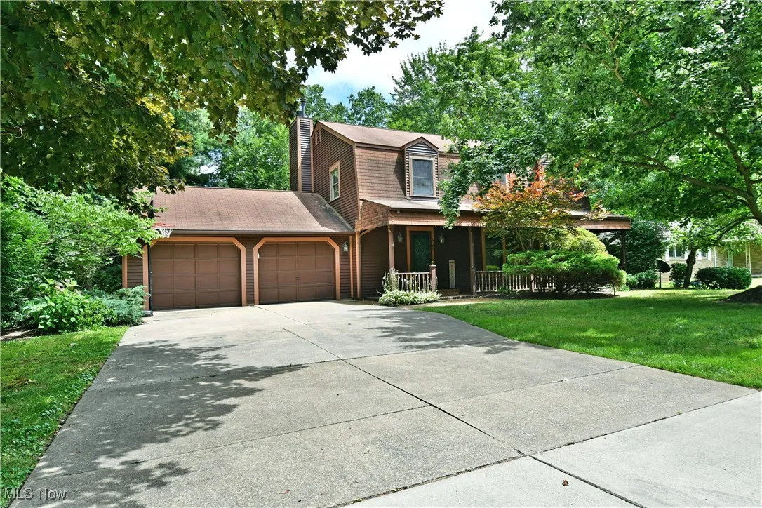 View of front of house featuring a gambrel roof, a front yard, a chimney, an attached garage, and concrete driveway