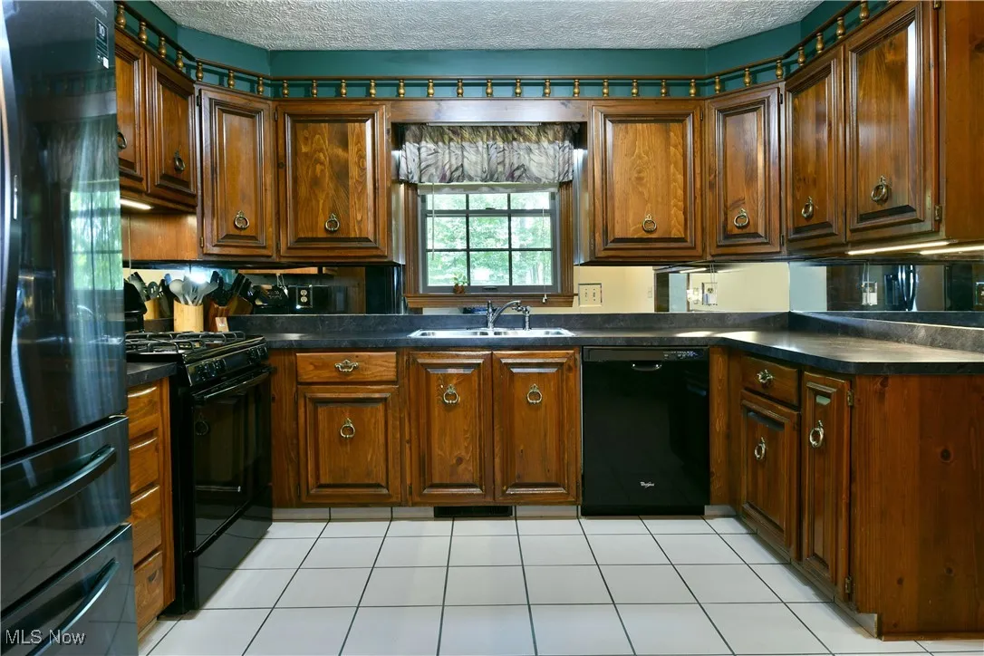 Kitchen with black appliances, dark countertops, a textured ceiling, light tile patterned floors, and brown cabinets