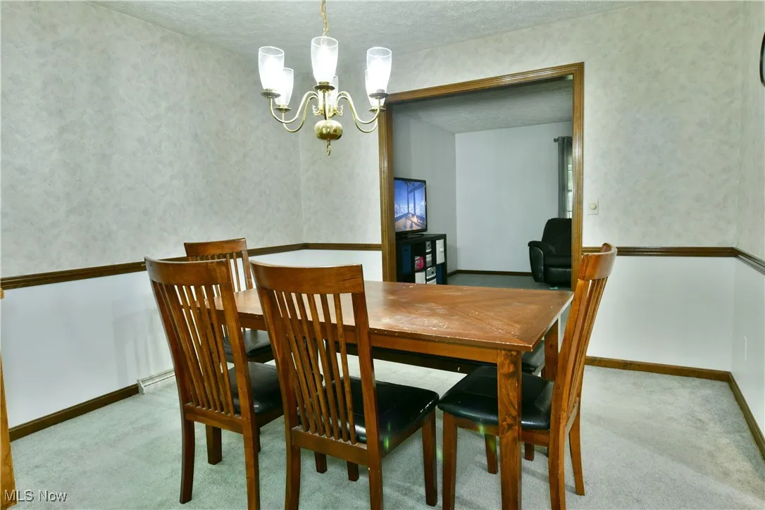 Carpeted dining space featuring a chandelier and a textured ceiling