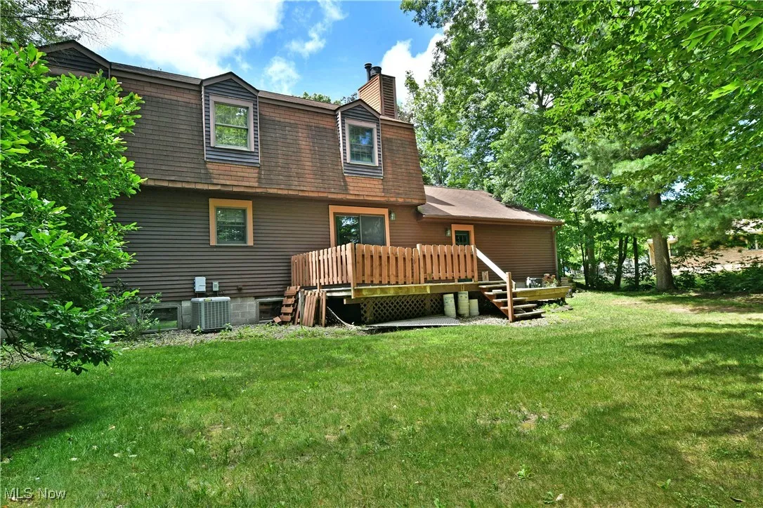 Back of property with a chimney, a lawn, a wooden deck, and a gambrel roof