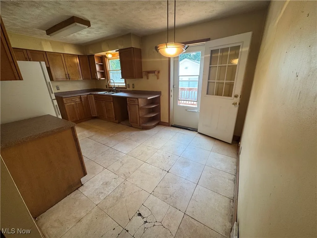 Kitchen featuring open shelves, freestanding refrigerator, dark countertops, a textured ceiling, and brown cabinetry