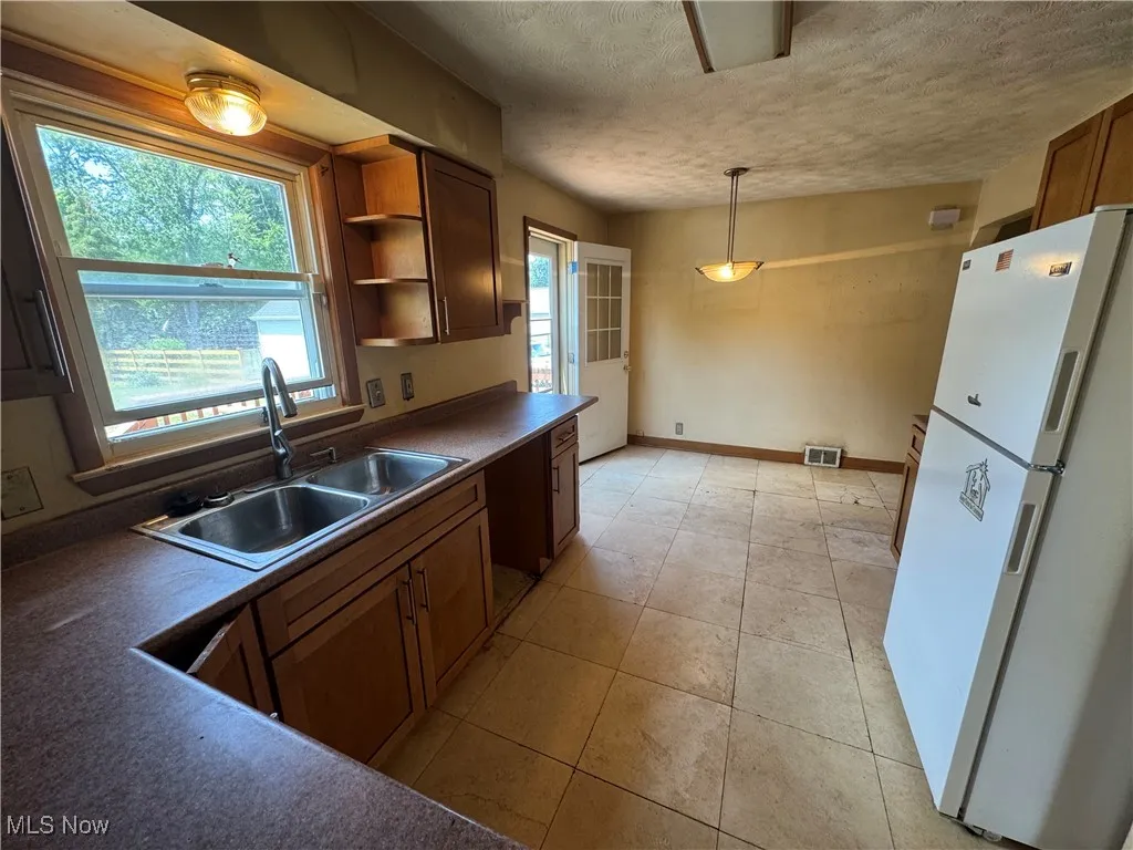Kitchen featuring freestanding refrigerator, dark countertops, a textured ceiling, light tile patterned flooring, and hanging light fixtures