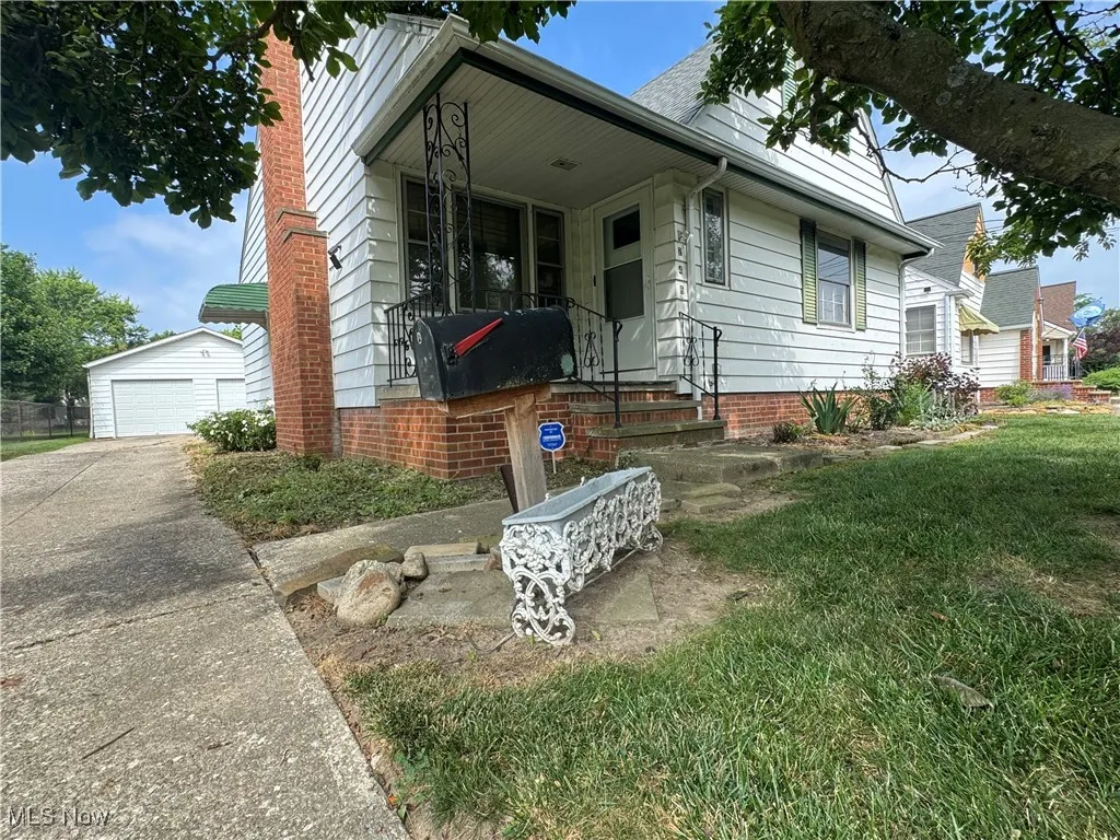View of front of home featuring an outbuilding, a garage, covered porch, a chimney, and a front lawn