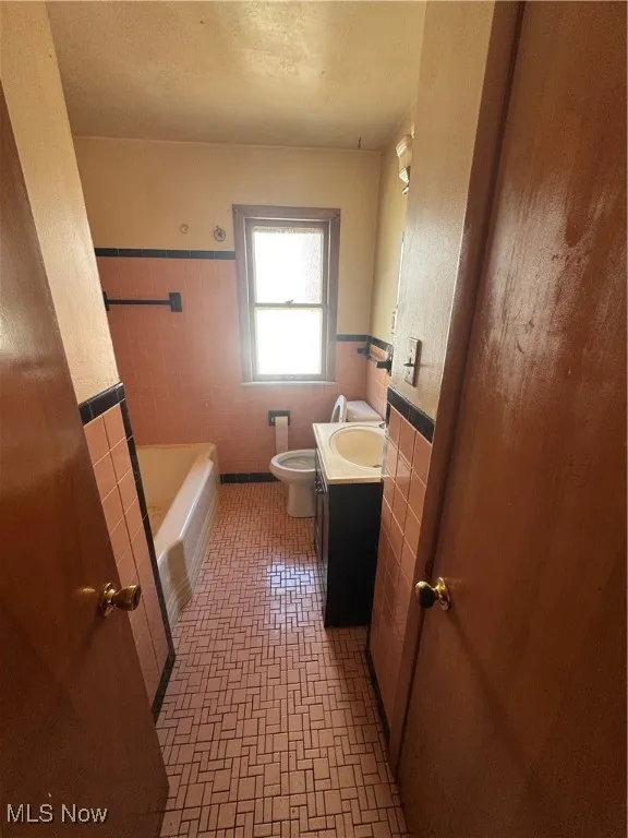 Bathroom with tile walls, vanity, a bathtub, and wainscoting