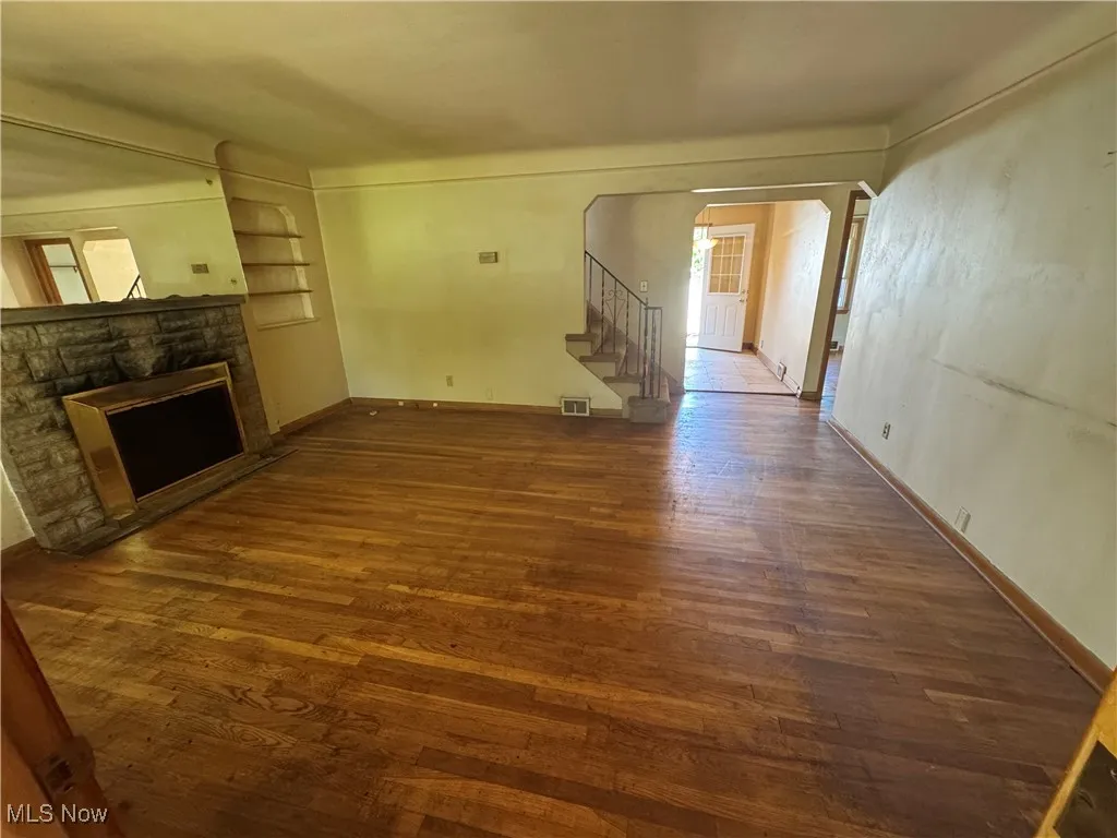 Unfurnished living room featuring stairs, wood finished floors, and a stone fireplace