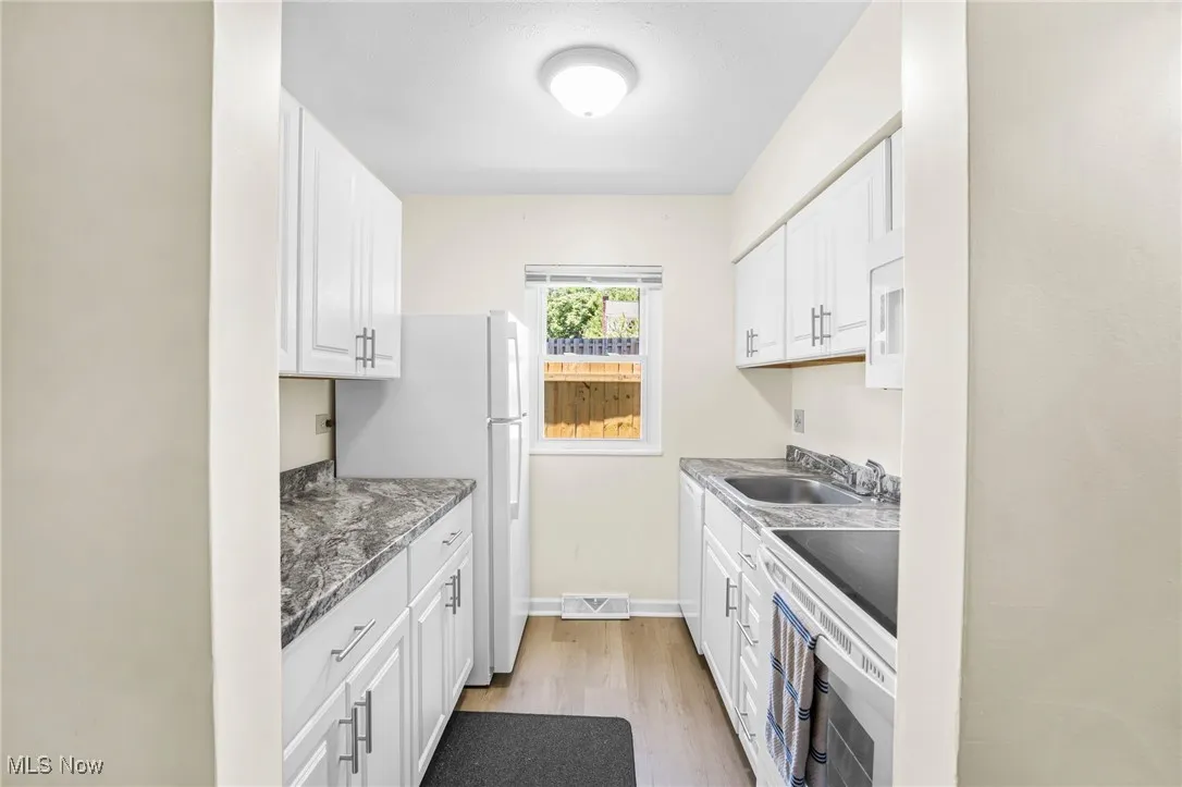 Kitchen with light wood-style floors, white cabinets, and white appliances