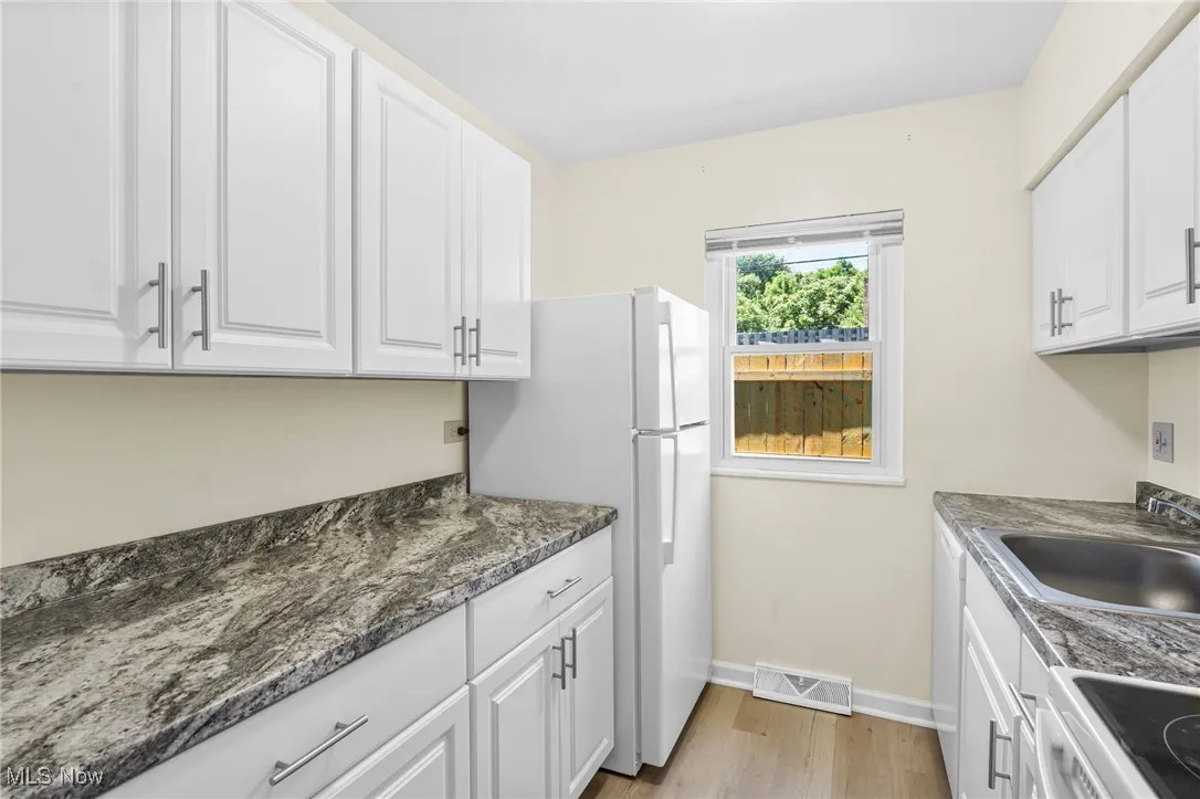 Kitchen featuring white cabinetry, light wood finished floors, white appliances, and dark stone counters