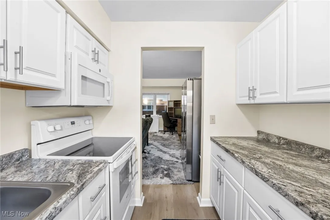 Kitchen with white appliances, light wood-style flooring, white cabinetry, and dark stone counters