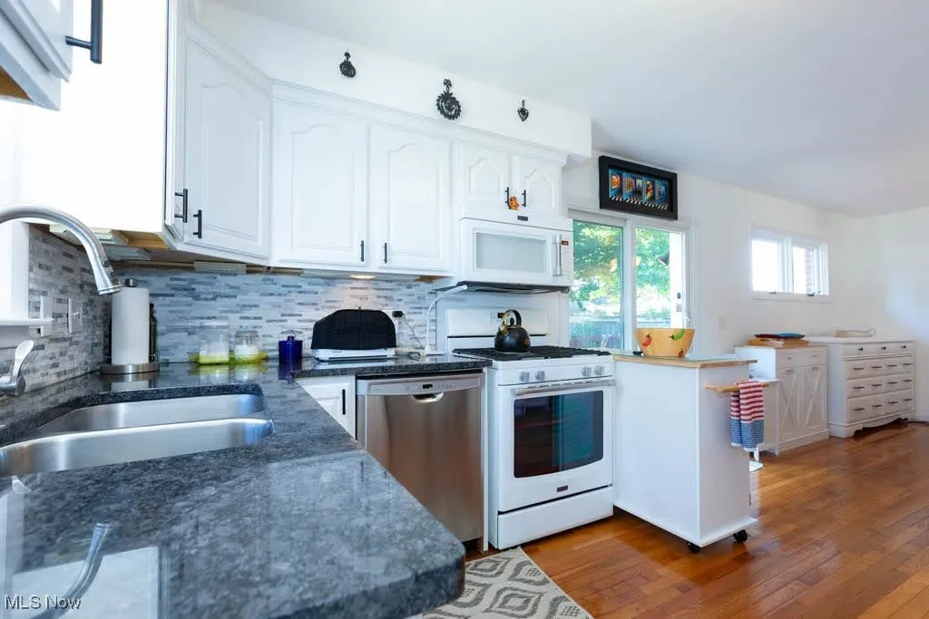 Kitchen featuring white appliances, dark wood finished floors, white cabinetry, tasteful backsplash, and dark stone counters
