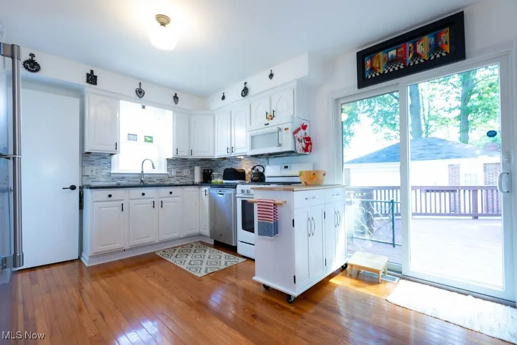 Kitchen featuring white appliances, light wood finished floors, white cabinets, decorative backsplash, and dark countertops