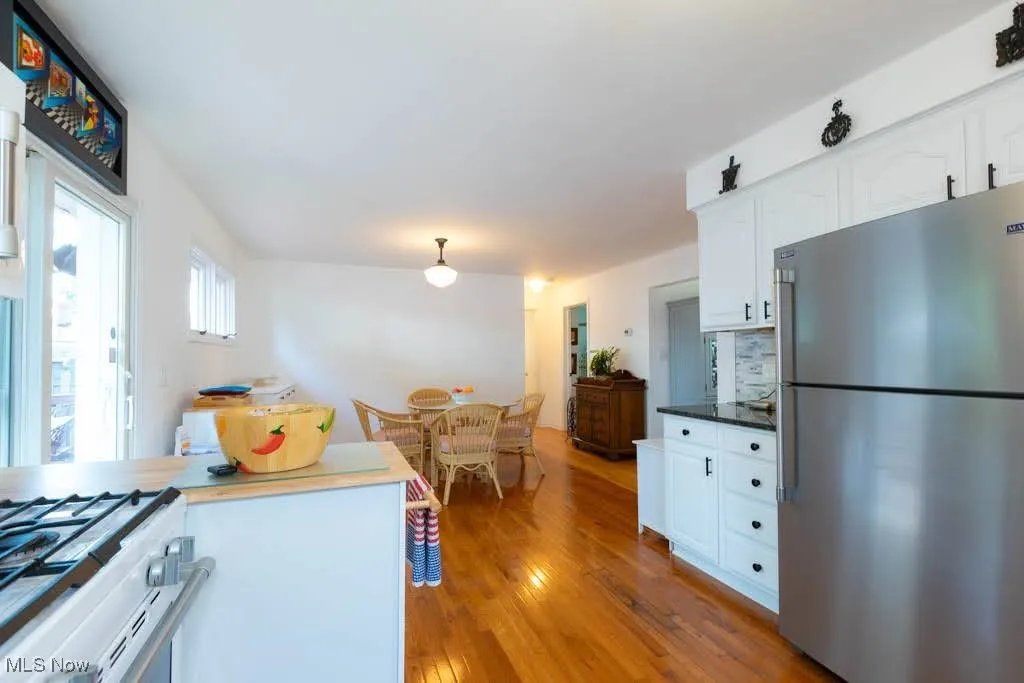 Kitchen with freestanding refrigerator, white cabinets, gas range gas stove, wood finished floors, and pendant lighting