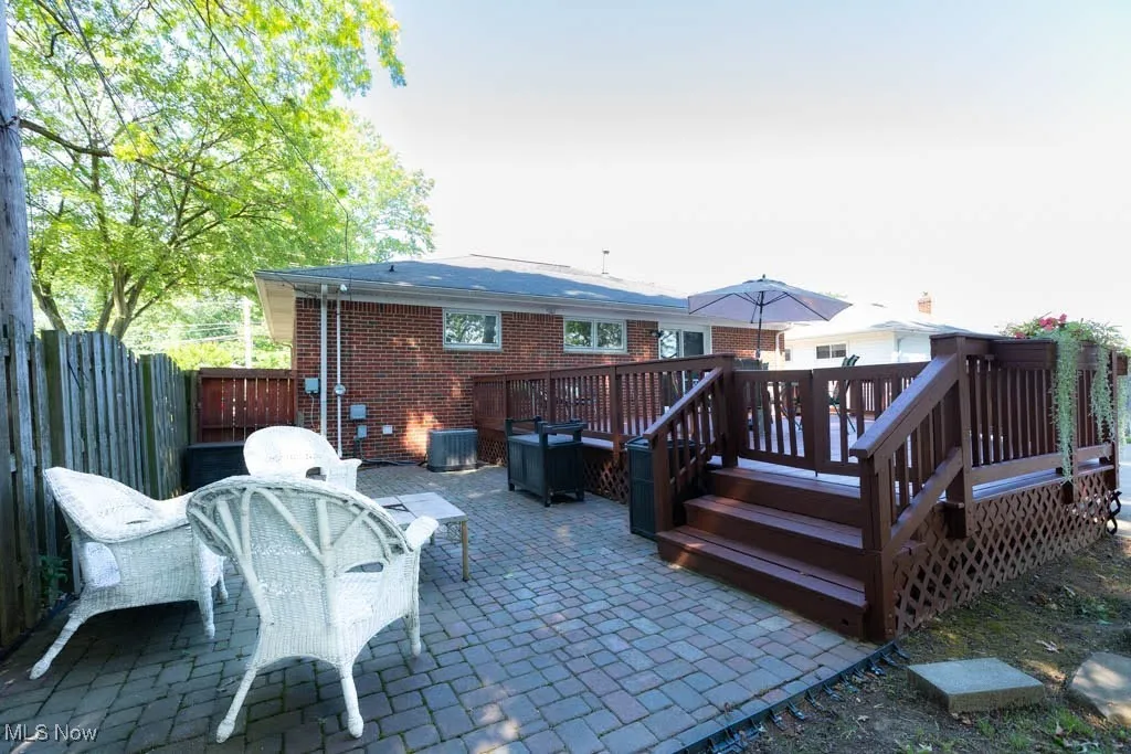 Back of property featuring a patio area, outdoor dining space, brick siding, and a wooden deck
