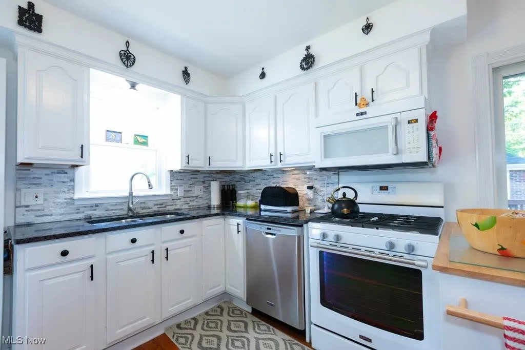 Kitchen featuring white appliances, white cabinetry, decorative backsplash, and dark stone countertops
