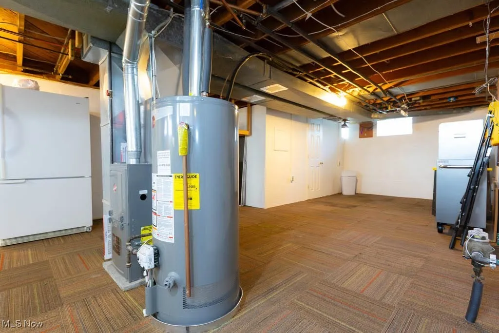 Below grade area THAT HAS BEEN WATERPROOFED. featuring freestanding refrigerator, water heater, and carpet flooring
