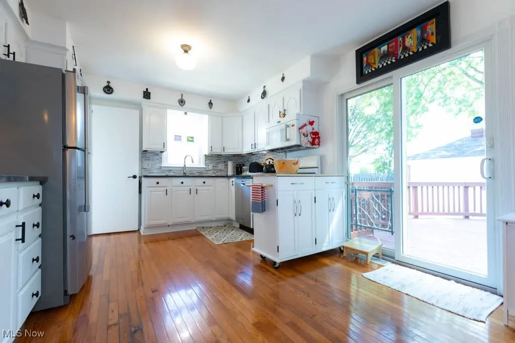 Kitchen featuring freestanding refrigerator, wood-type flooring, white cabinetry, and tasteful backsplash