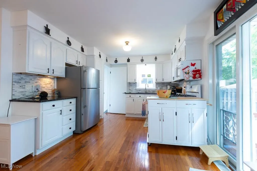 Kitchen with white cabinets, tasteful backsplash, wood finished floors, freestanding refrigerator, and range