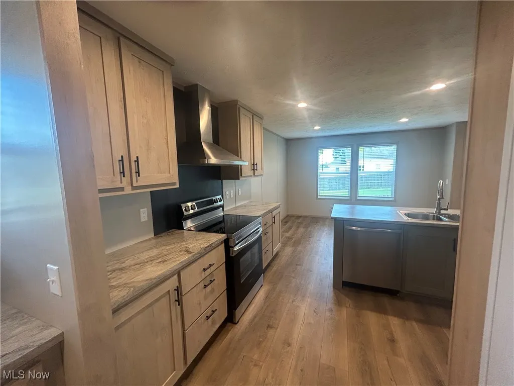 Kitchen featuring stainless steel appliances, wall chimney exhaust hood, light wood finished floors, and recessed lighting