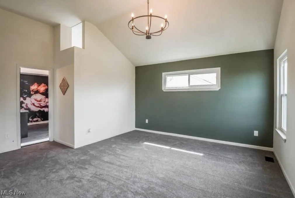 Unfurnished room with dark carpet, plenty of natural light, a chandelier, and lofted ceiling