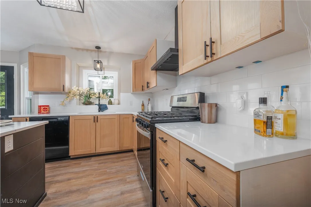 Kitchen featuring stainless steel range with gas cooktop, wall chimney range hood, light wood-style flooring, backsplash, and dishwasher