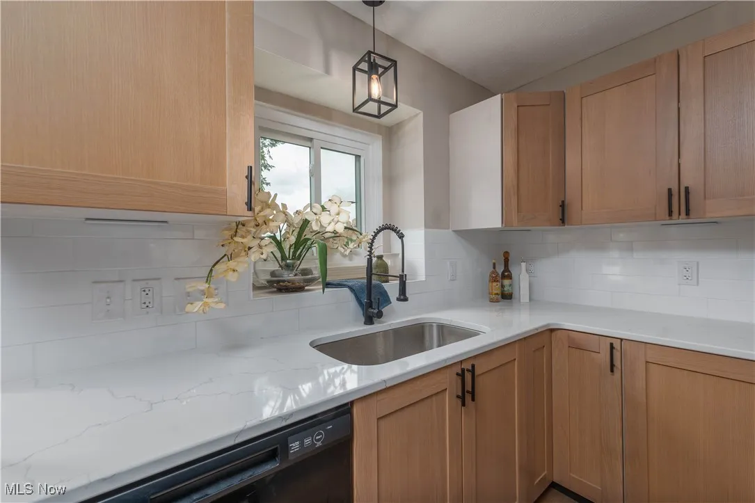 Kitchen with black dishwasher, tasteful backsplash, light stone counters, and decorative light fixtures