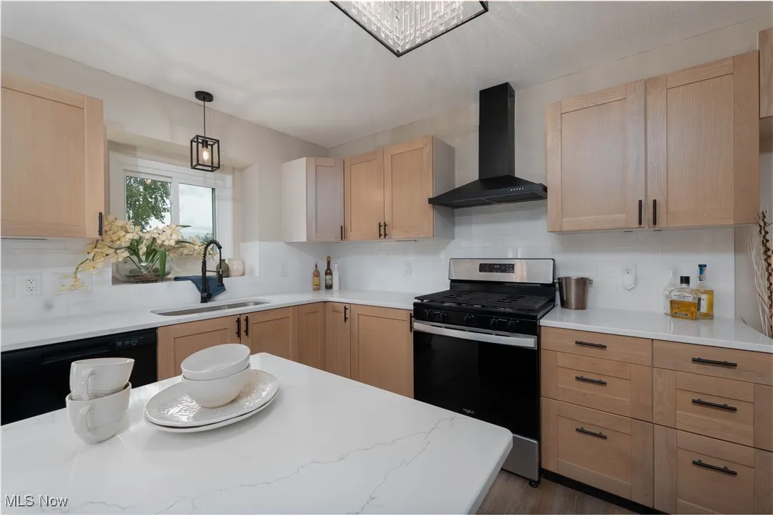 Kitchen featuring light brown cabinets, stainless steel gas range, wall chimney range hood, and decorative backsplash