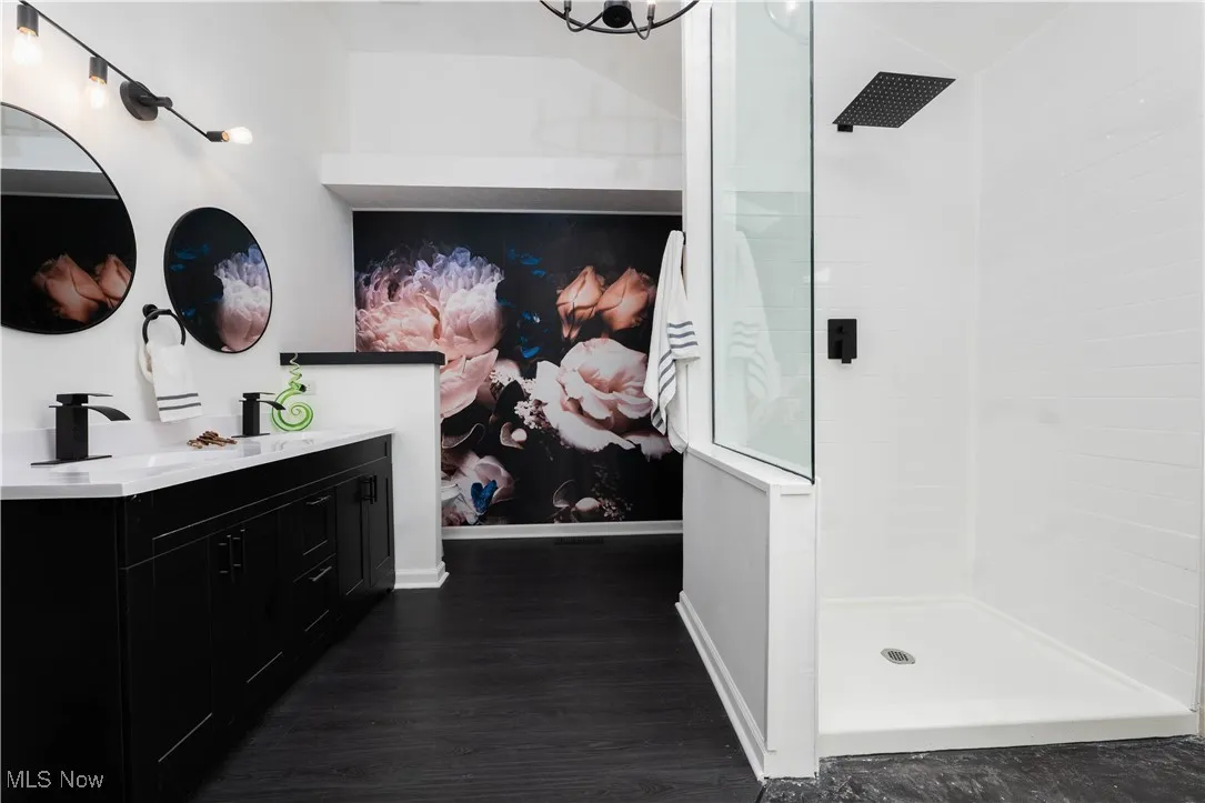 Bathroom featuring tiled shower, double vanity, and wood finished floors