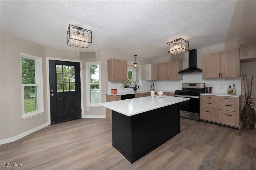 Kitchen featuring light countertops, stainless steel range with gas cooktop, wall chimney range hood, a chandelier, and a textured ceiling