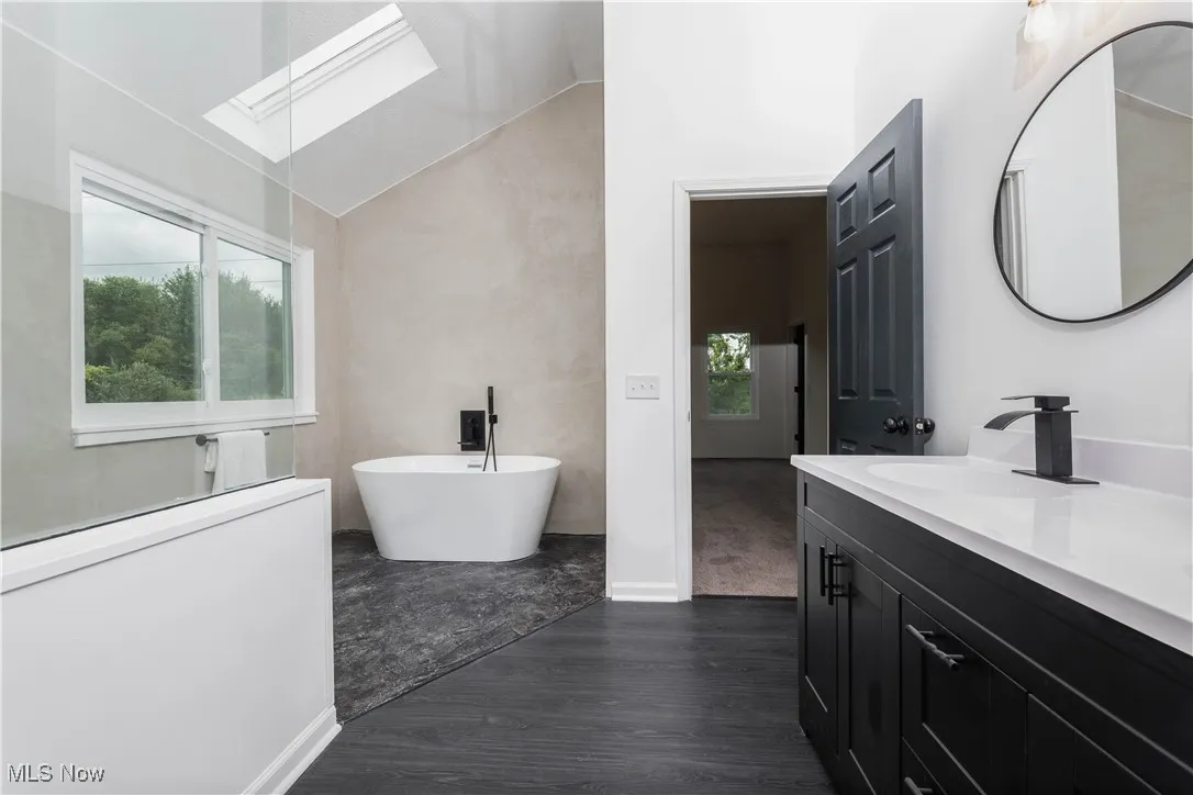 Bathroom featuring a skylight, vanity, a soaking tub, plenty of natural light, and vaulted ceiling