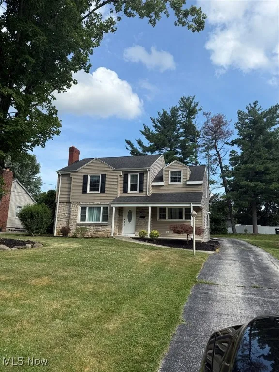 View of front facade with a chimney, stone siding, a front yard, and a porch