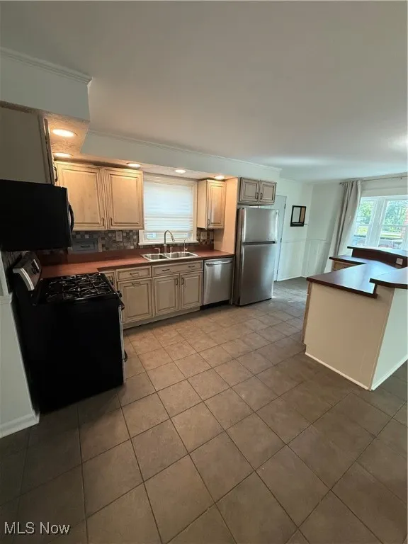 Kitchen with range, fridge, stainless steel dishwasher, tile patterned flooring, and dark countertops