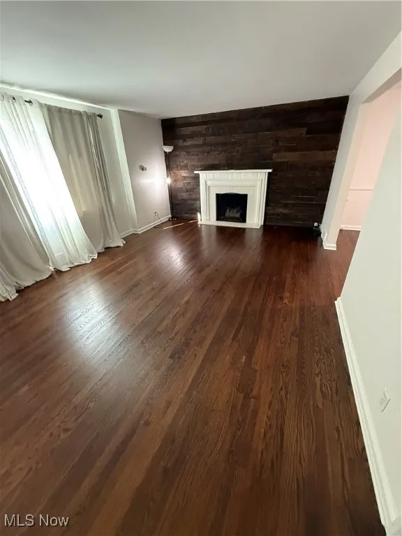 Unfurnished living room with a fireplace, dark wood-style flooring, and wooden walls