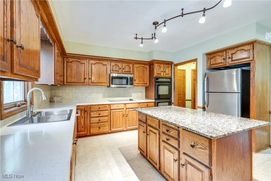 Kitchen featuring black appliances, decorative backsplash, brown cabinets, and a kitchen island
